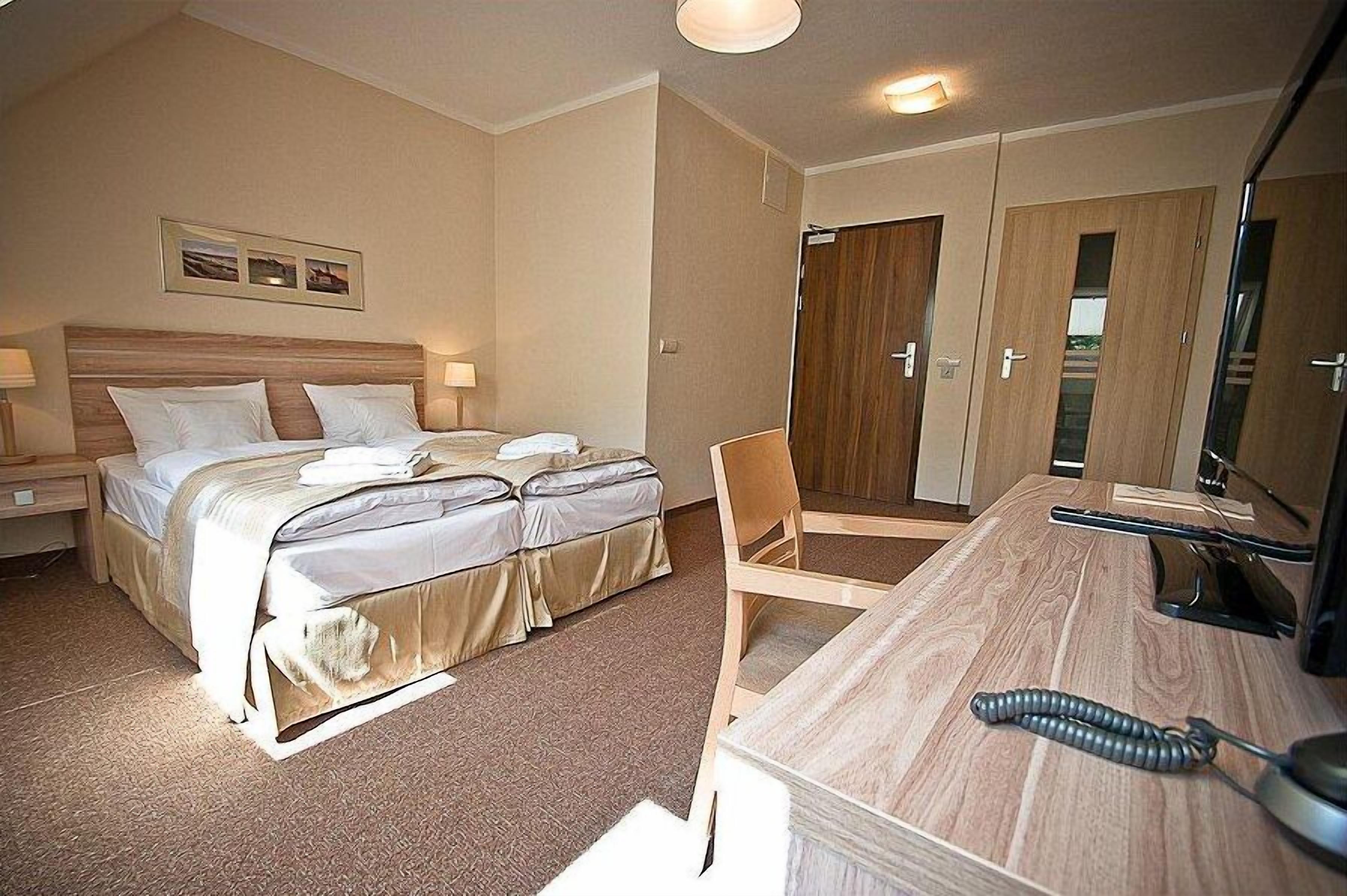 A hotel room with a bed, bedside tables, a desk, a chair, and a mirror.