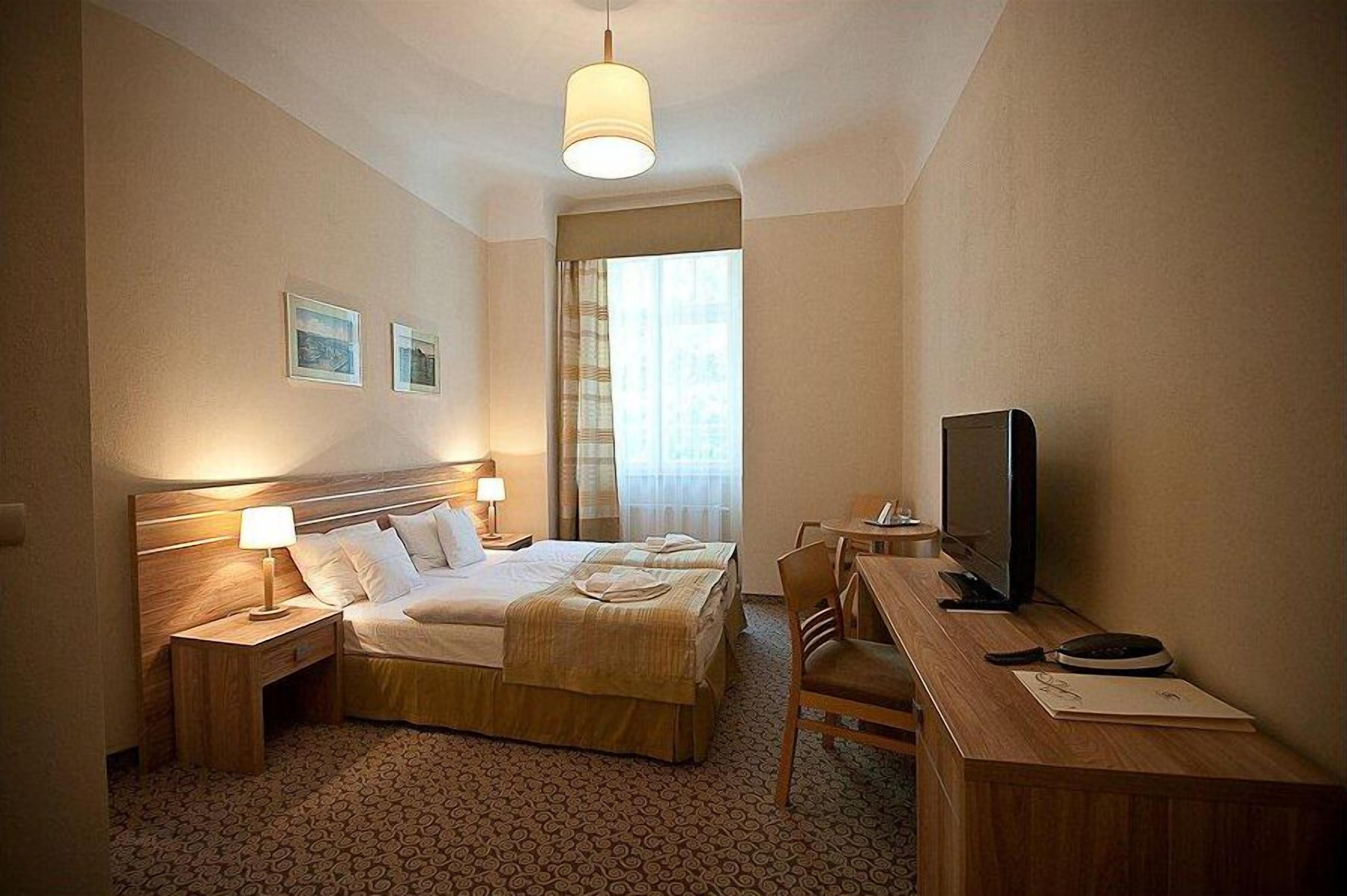 A hotel room with a double bed, bedside lamps, a desk with a television, and a window with curtains.