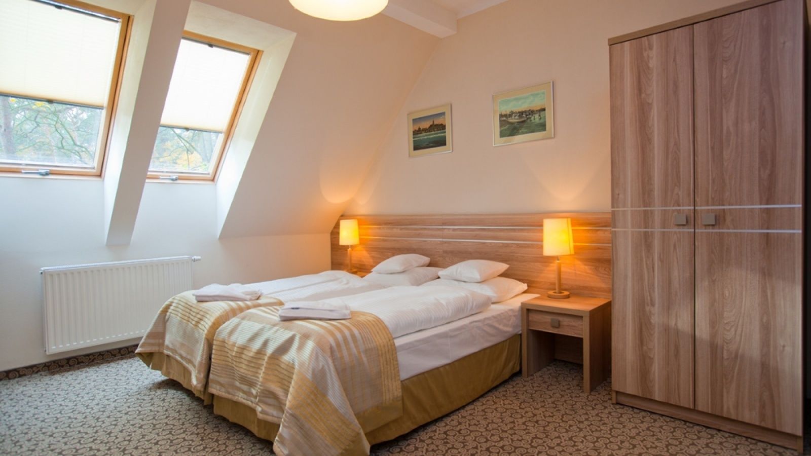 A bedroom with a bed, two bedside lamps, a wardrobe, and two framed pictures on the wall.