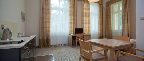 A compact hotel room with a kitchenette, a dining area, and a TV.