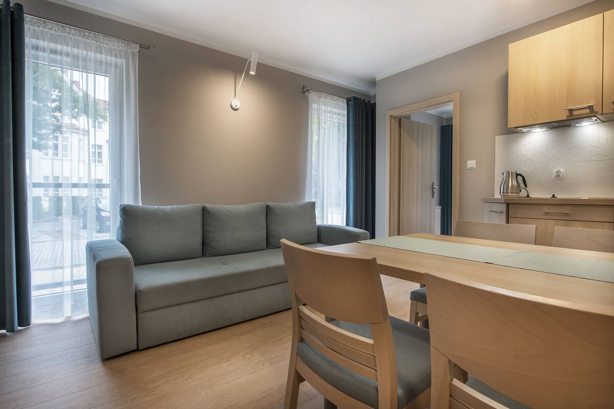 Ett modernt vardagsrum med en soffa, ett matbord och stolar. Det finns också ett köksområde med skåp och en vattenkokare.