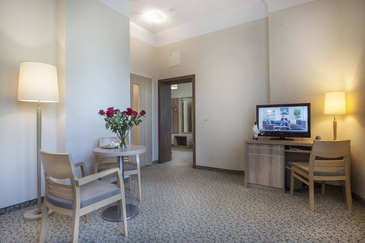 Ett hotellrum med ett skrivbord, två stolar, en tv och en vas med blommor.