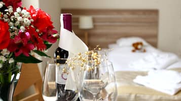 A hotel room with a bed, a bedside table with a vase of flowers, two wine glasses, and a bottle of wine.