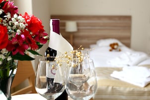 A hotel room with a bed, a bedside table with a vase of flowers, two wine glasses, and a bottle of wine.