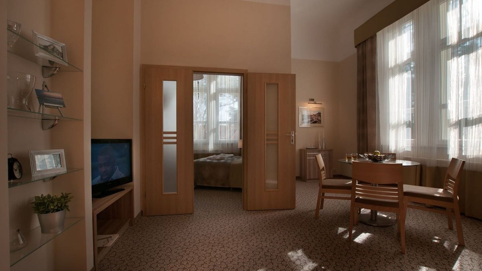 A hotel room with a bed, a TV, a dining area, and a small kitchen.
