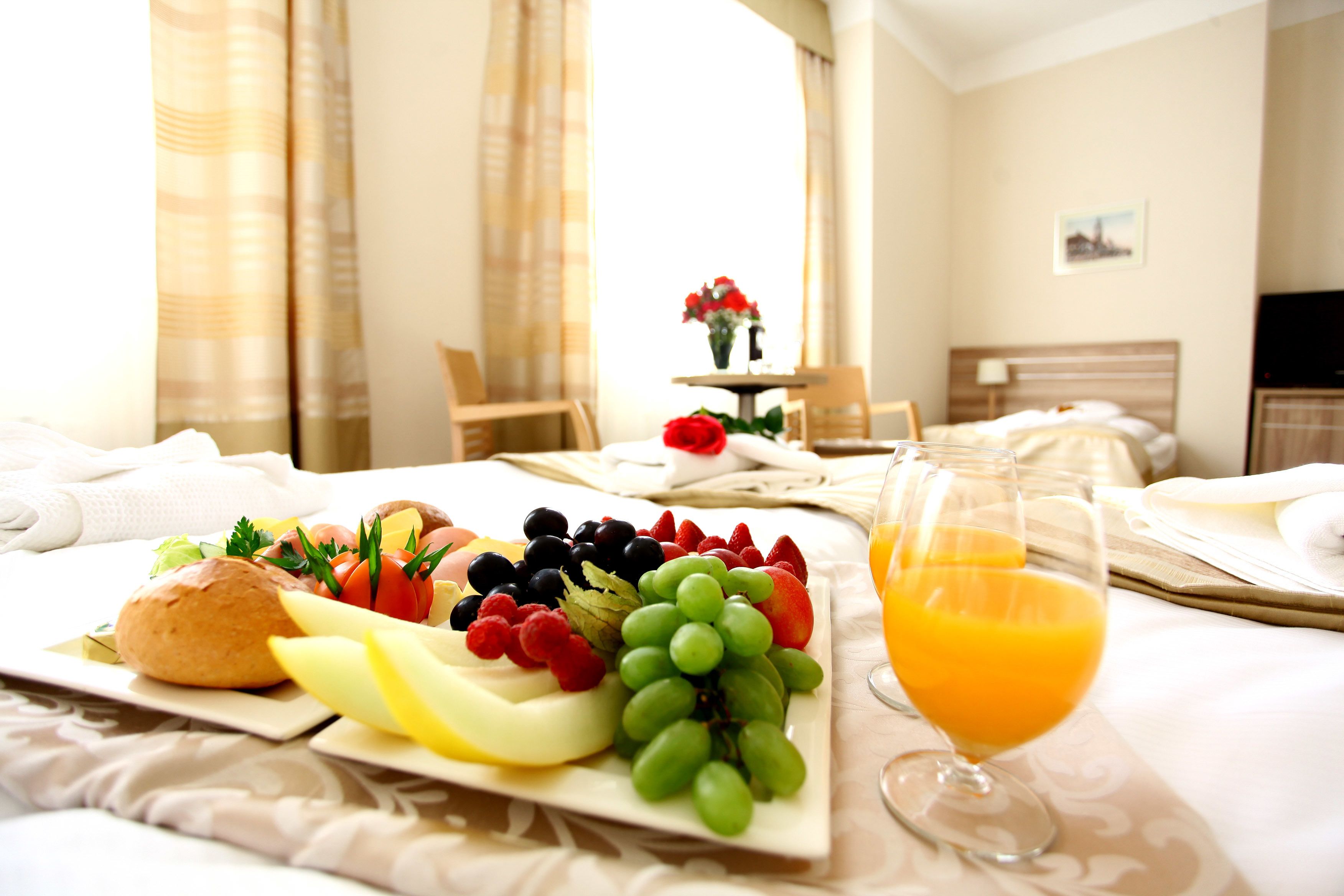 Ein Frühstücksbuffet mit Obstplatte, Toast und Orangensaft auf einem Hotelbett.