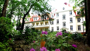 A building with multiple windows and balconies, surrounded by greenery and trees. - Hotel Cesarskie Ogrody (Swinoujscie)