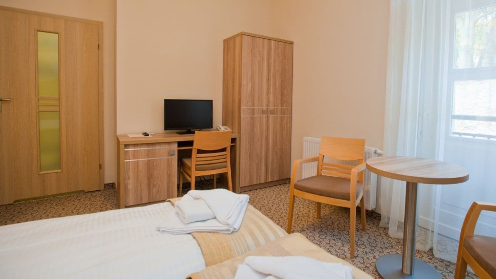 Une chambre d’hôtel comprenant un lit, un bureau avec un ordinateur, une chaise et une petite table.