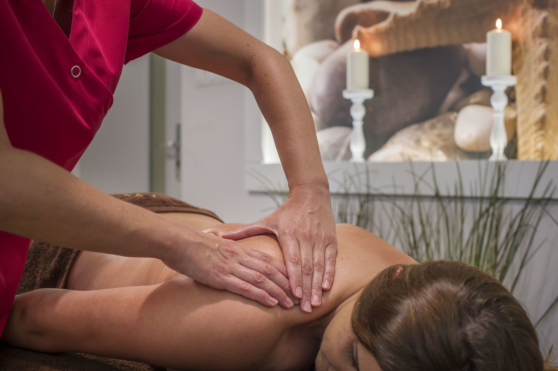 A massage therapy session in a room with a bed, candles, and a plant.
