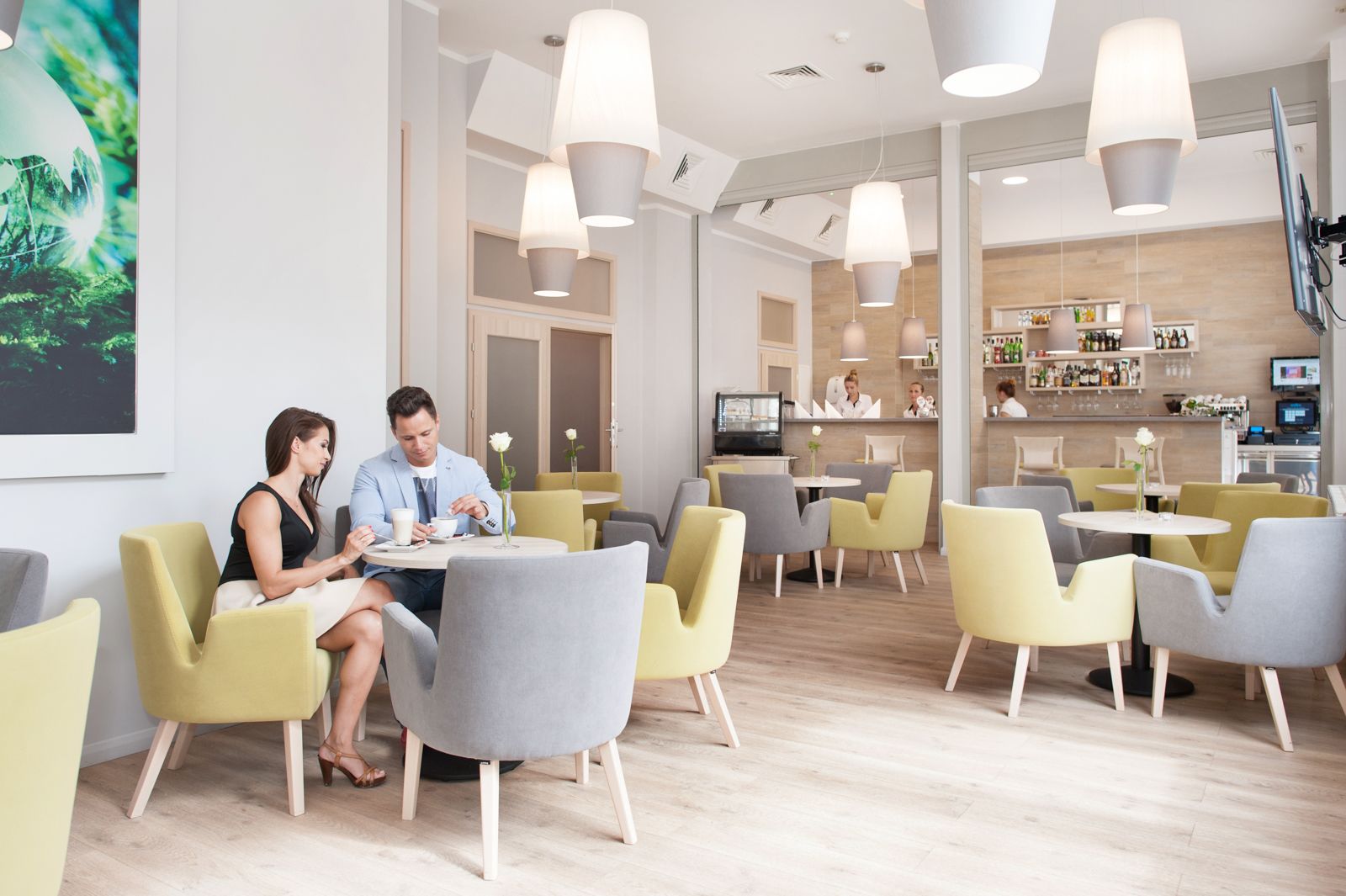 Een moderne eetruimte met gele en grijze stoelen, een bar op de achtergrond en een groot schilderij aan de muur.