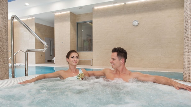 A man and a woman in a hot tub with a tiled wall and a clock in the background. - Hotel Cesarskie Ogrody (Swinoujscie)