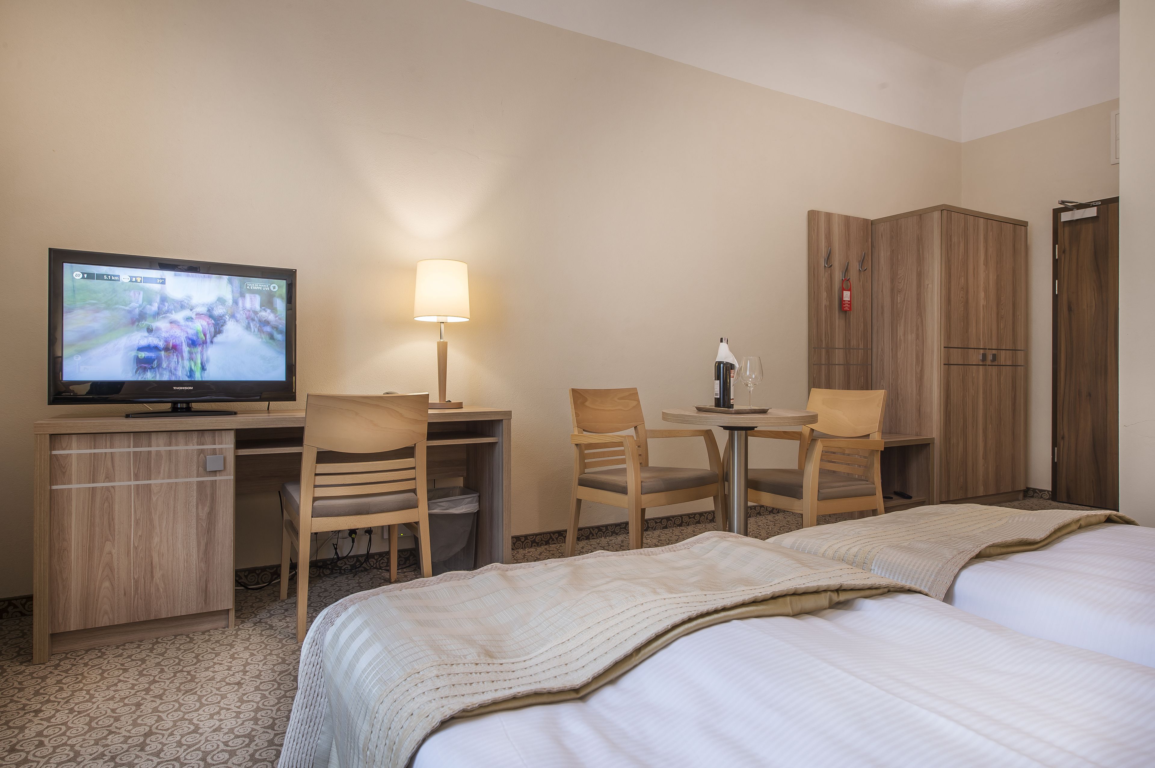 Una habitación de hotel con dos camas, un escritorio con televisor, una lámpara y un armario.