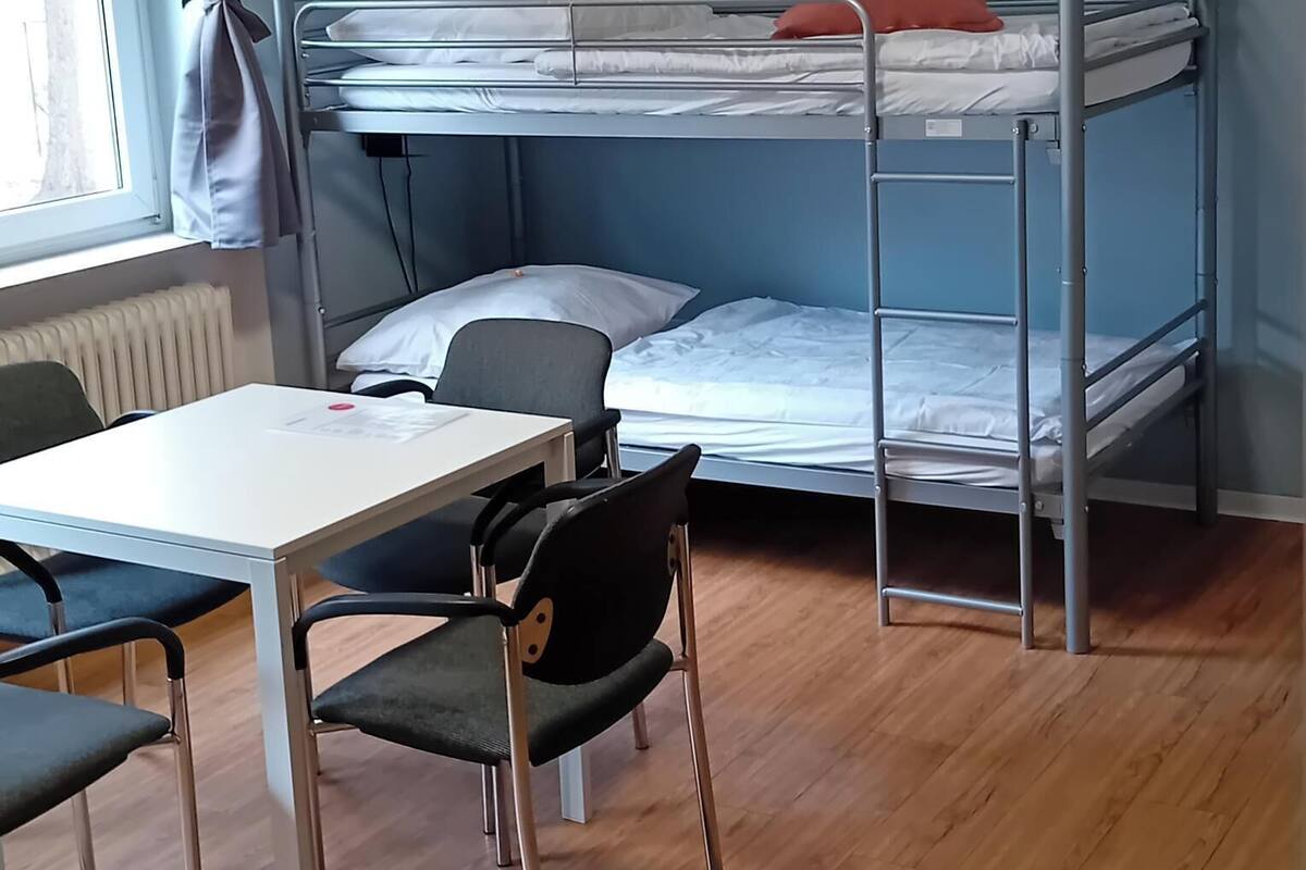 A bunk bed room with a table and chairs, a radiator, and a window with curtains.