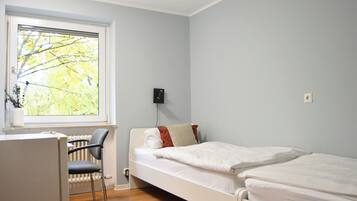 A bedroom with a single bed, a chair, a radiator, and a window with a view of trees.