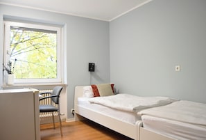 A bedroom with a single bed, a chair, a radiator, and a window with a view of trees. - 1/2/sleep Hostel Nürnberg Messe (Nuremberg)