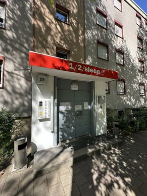 A building with a sign indicating 1/2 sleep rooms, a door labeled 'Box 1/2', and a trash bin. - 1/2/sleep Hostel Nürnberg Messe (Nuremberg)