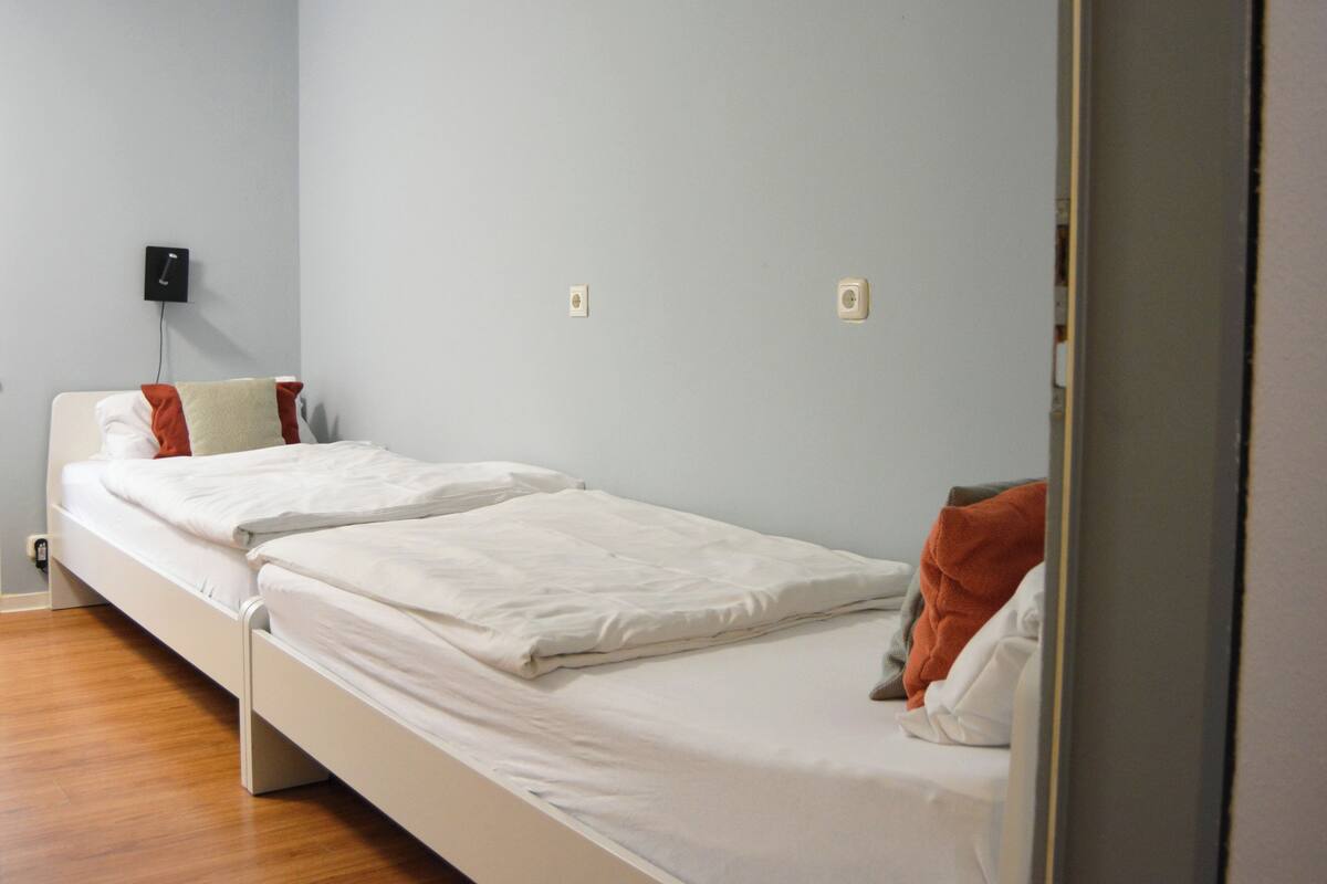 A single-bed room with a wooden floor, a white bed, and a light blue wall.