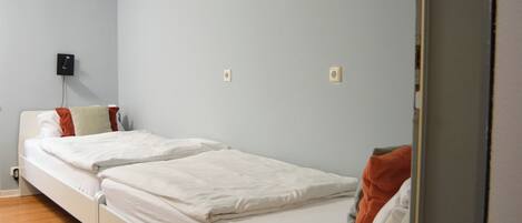Une chambre avec un lit simple, un plancher en bois, un lit blanc et un mur bleu clair.