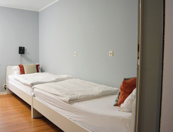 A single-bed room with a wooden floor, a white bed, and a light blue wall. - 1/2/sleep Hostel Nürnberg Messe (Nuremberg)