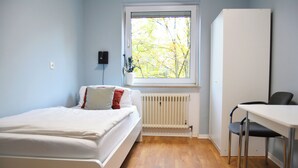 A bedroom with a bed, a radiator, a window with a view of trees, and a desk with a chair. - 1/2/sleep Hostel Nürnberg Messe (Nuremberg)