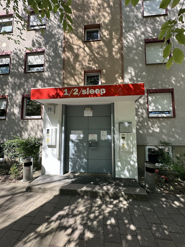 A building entrance with a sign indicating 1/2/ sleep accommodation, a door with a keycard slot, and a trash bin. - 1/2/sleep Hostel Nürnberg Messe (Nuremberg)