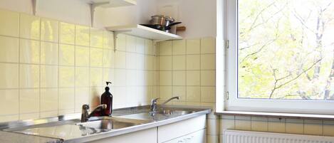 A kitchen with white cabinets, a stainless steel sink, and a window with a view of trees.