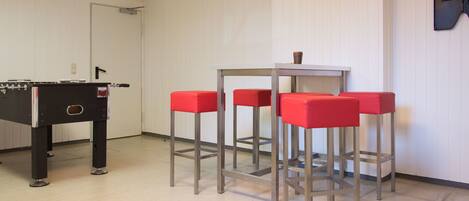 A room with a foosball table, four red bar stools, and a small table with a cup.
