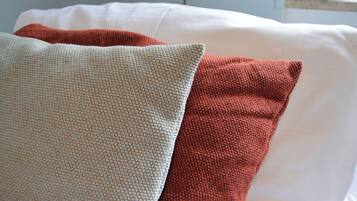 Ein Bett mit weißer Bettwäsche und zwei Kissen, eines mit Punkten und das andere schlicht rot.