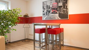 A modern kitchen with wooden flooring, a red and white wall, a bar area with red stools, and a large black and white photograph of a street scene. - 1/2/sleep Hostel Nürnberg Messe (Nuremberg)