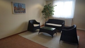 Una sala de estar con un sofá, dos sillones, una mesa de centro de vidrio, un cuadro en la pared, una planta en maceta y una ventana con cortinas.