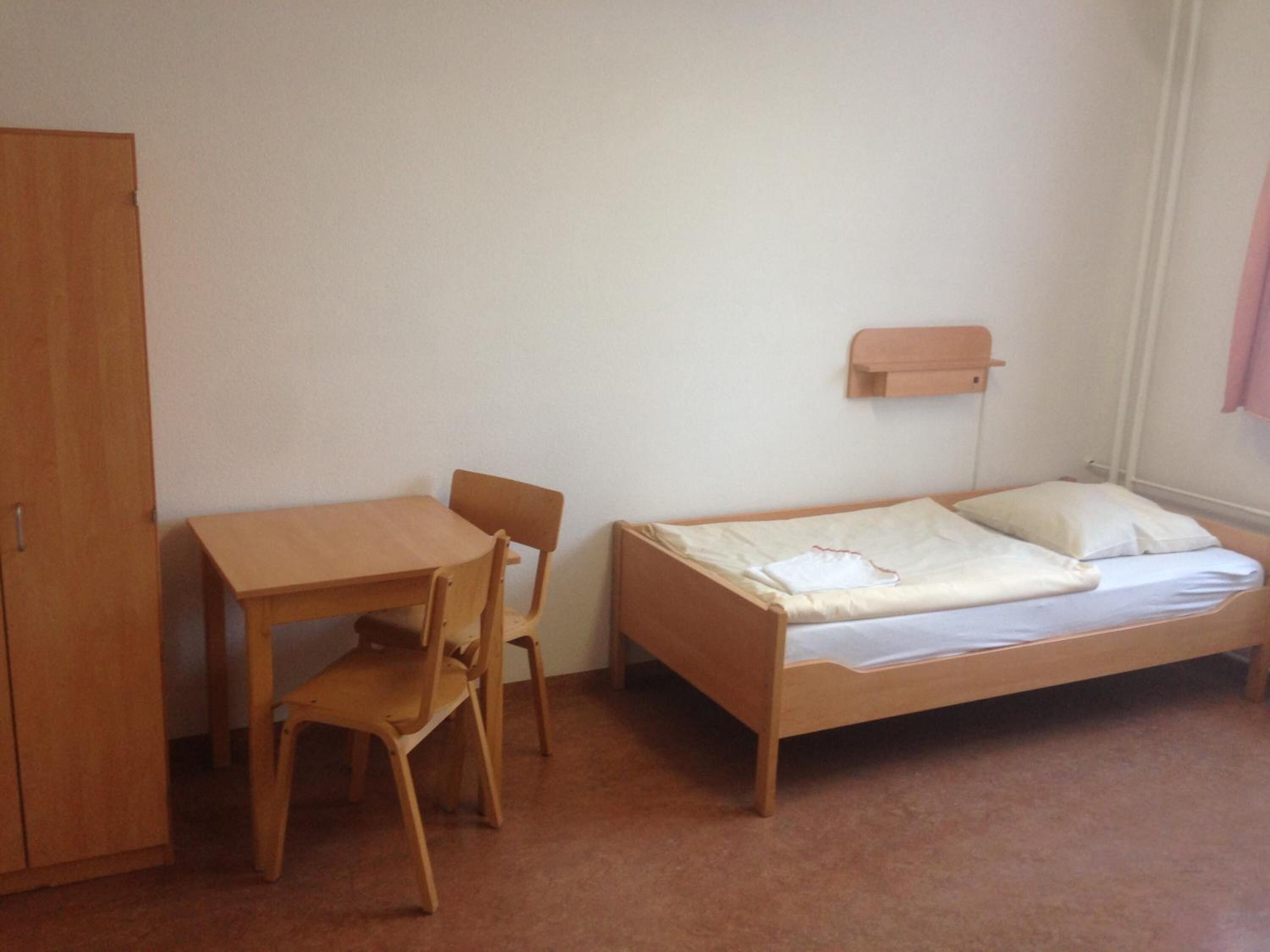 Una habitación pequeña con un escritorio de madera, una silla y una cama individual con colchón y almohadas.