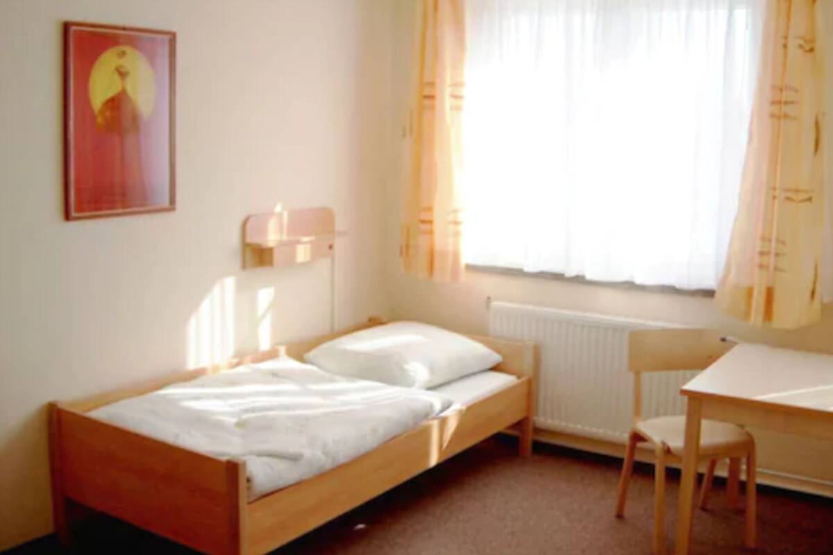 A small, single-bed room with a wooden bed, a desk, and a chair.