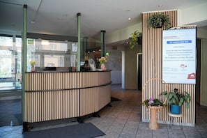 A reception desk with a modern design, a digital information board, and potted plants. - JUGENDGASTEHAUS DRESDEN - Hostel (Dresden)