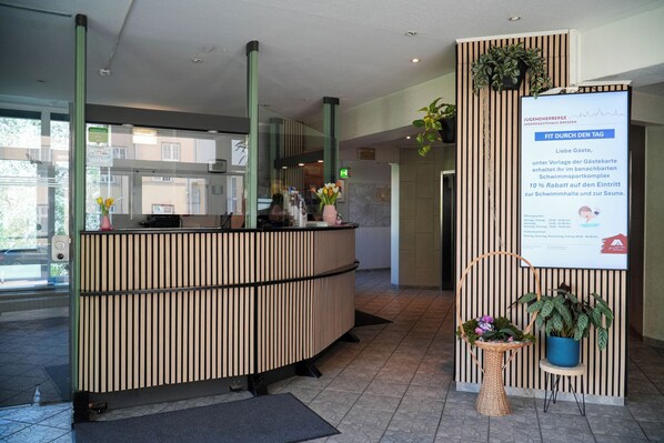 A reception desk with a modern design, a digital information board, and potted plants.