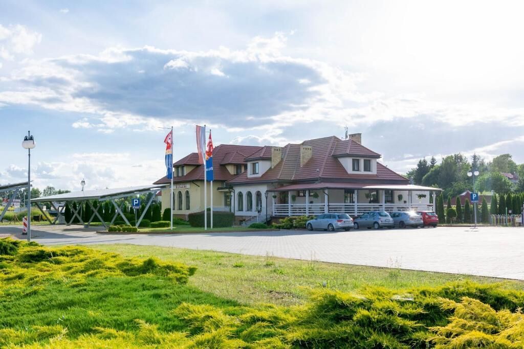 A large building with multiple flags, a covered walkway, and several parked cars.