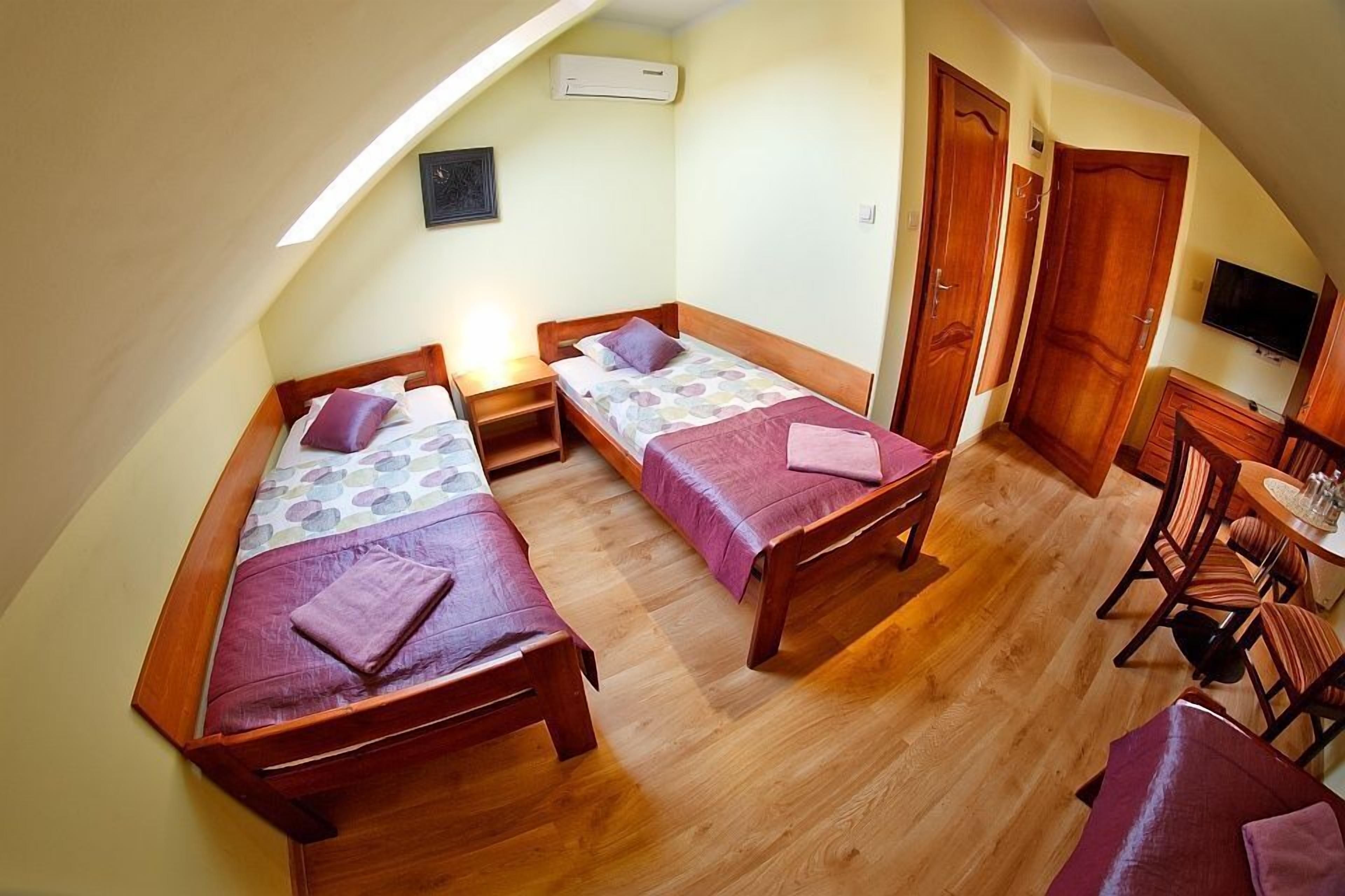 A dormitory room with two wooden beds, a small table, and a television.