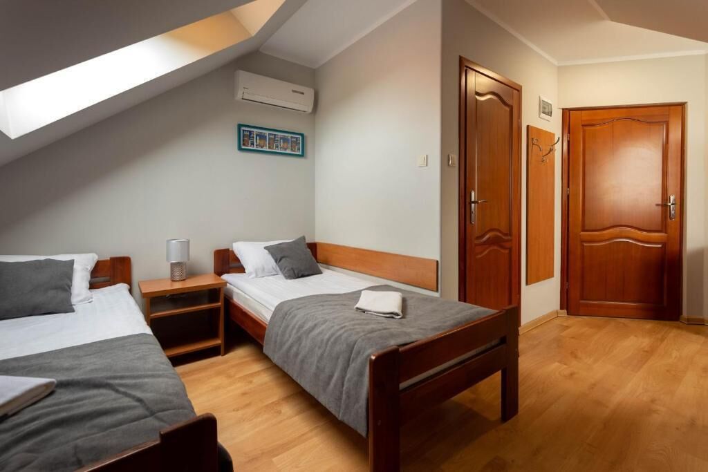 A bedroom with two beds, a wooden wardrobe, a bedside table with a lamp, and a picture on the wall.
