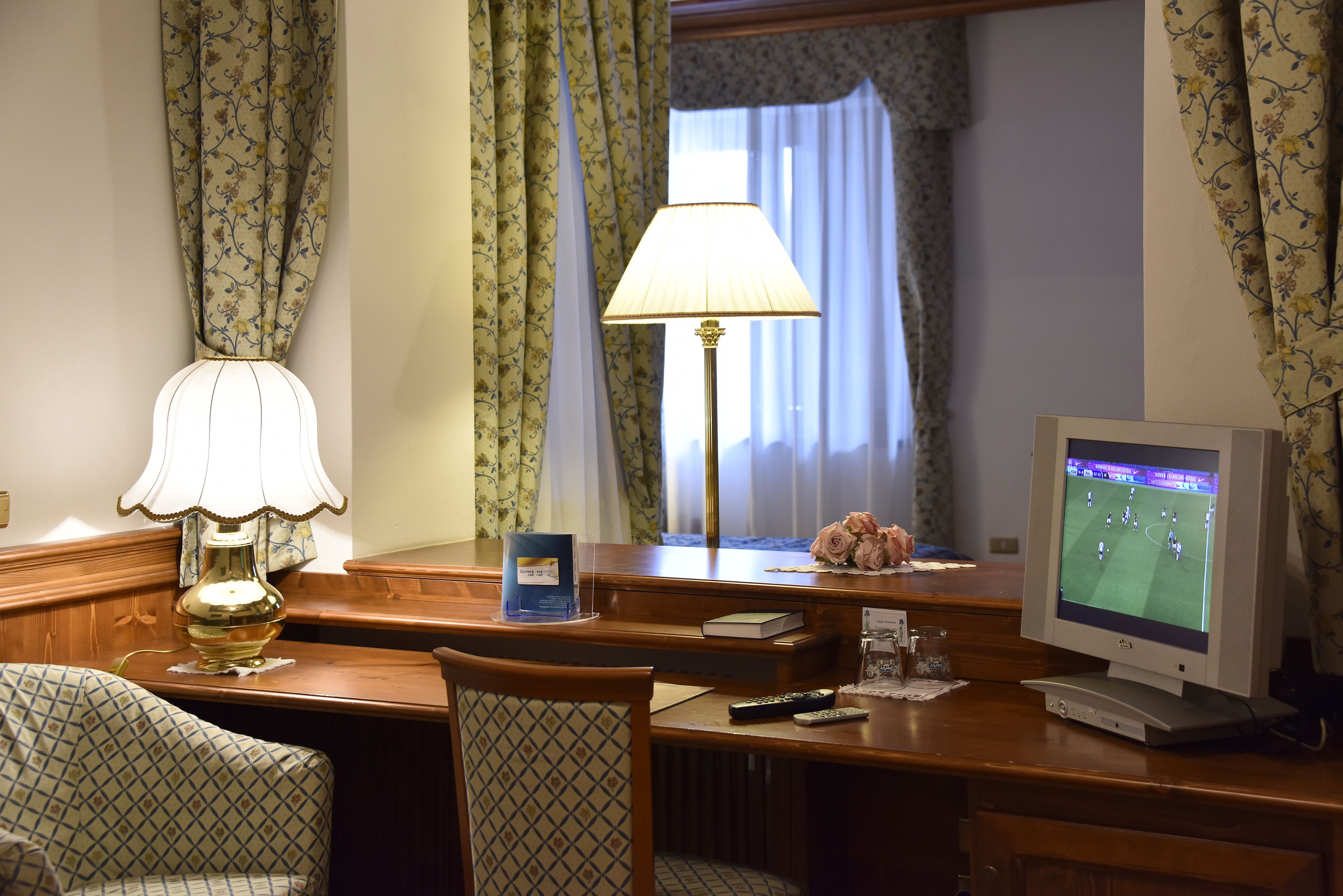 Una habitación de hotel con un escritorio de madera, una lámpara, un televisor y una silla.
