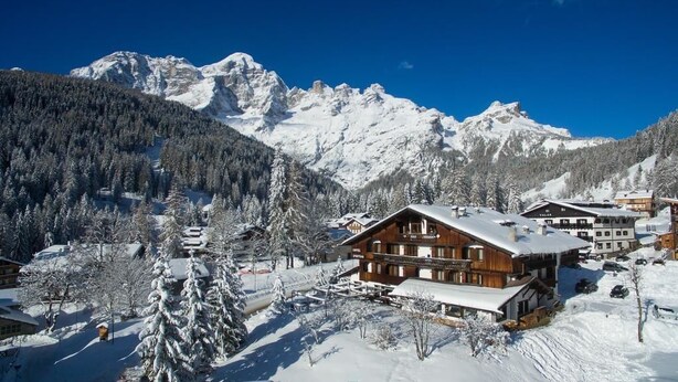 A snow-covered mountain resort with wooden buildings and a ski slope. - Hotel Sporting (Val di Zoldo)