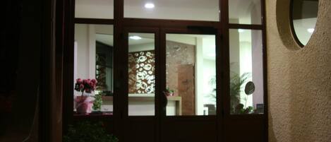 Entrada de hotel con una puerta de madera grande, una planta en maceta y un espejo redondo en la pared.
