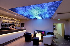 A bar area with a digital ceiling display, seating, and a counter with bottles. - Hôtel Bel Horizon (Saint-Chely-d'Apcher)