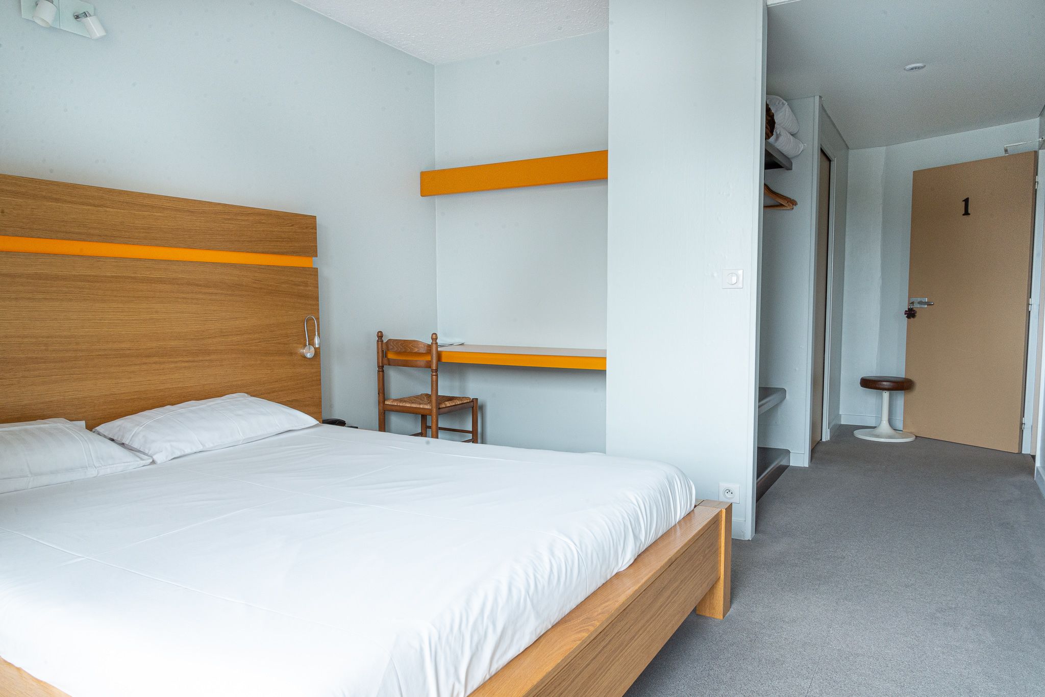 A bedroom with a wooden bed, a chair, and a small stool.
