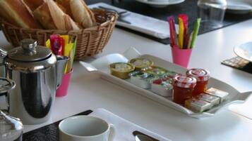 A breakfast table with bread, pastries, condiments, and a coffee pot.