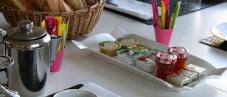 A breakfast table with bread, pastries, condiments, and a coffee pot.