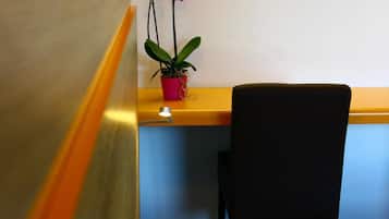 A hotel room with a bed, a desk, a chair, and a potted orchid.