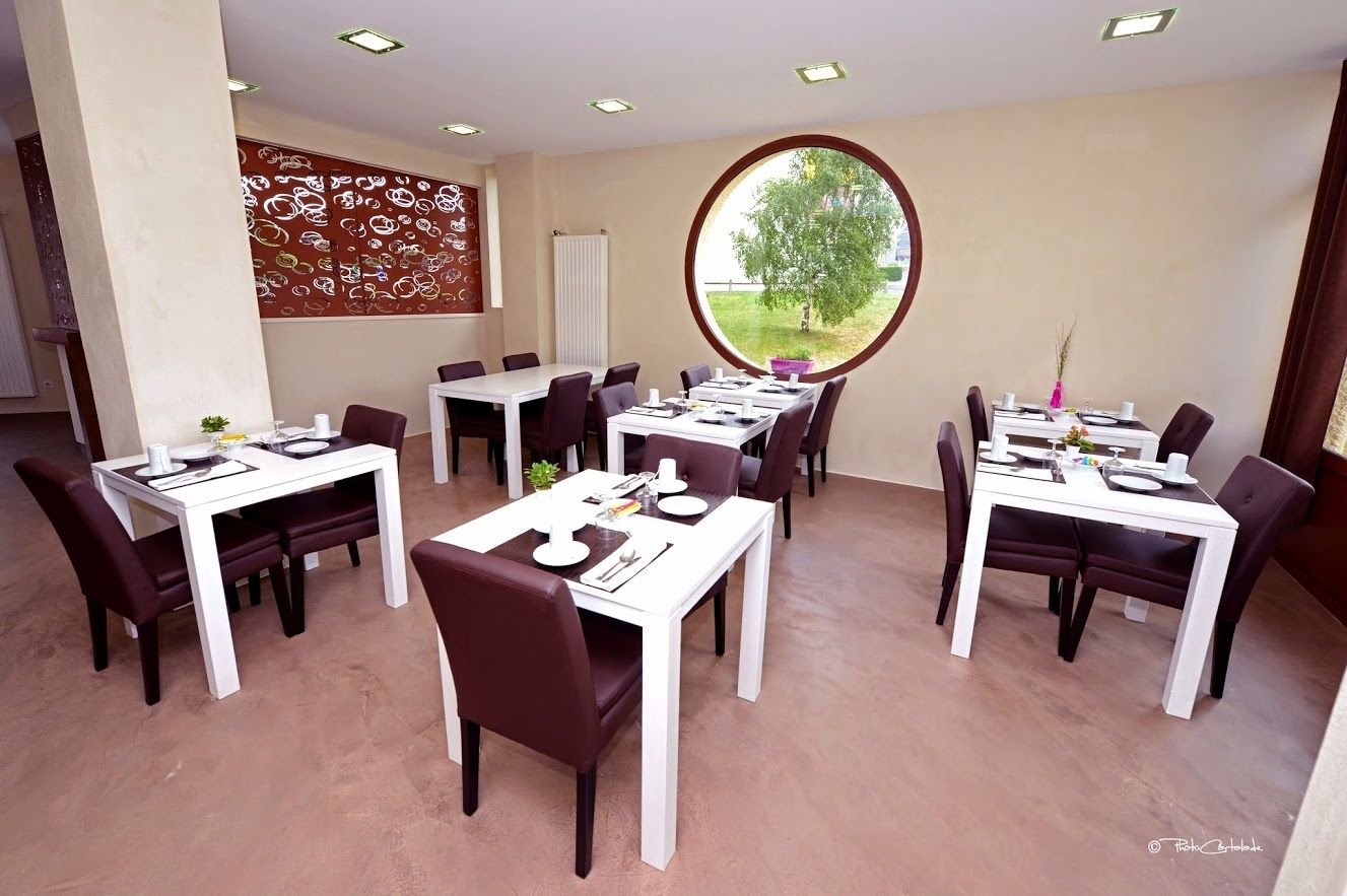 Un comedor con varias mesas y sillas, un muro decorativo y un amplio ventanal con vistas a la vegetación.