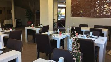 A restaurant with white tables and dark chairs, each set with cutlery and a small vase of flowers.