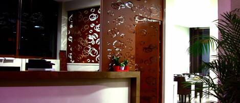 Un área de recepción con un escritorio de madera, una planta en maceta y una pared decorativa con patrones circulares.