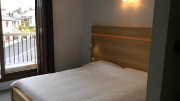 Una habitación de hotel con cama, ventana con cortinas e iluminación en la pared.
