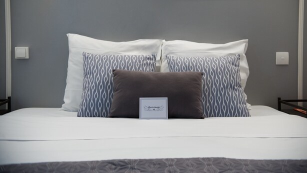 Una cama bien hecha con almohadas blancas y estampadas, una pequeña señal en la cama y un cabecero gris.